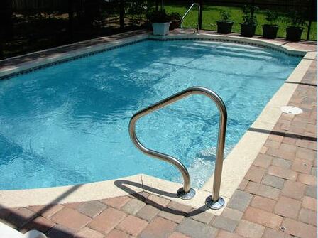 Picture of a nice clean pool with a hand rail for getting in and out with a nice tiled pool deck